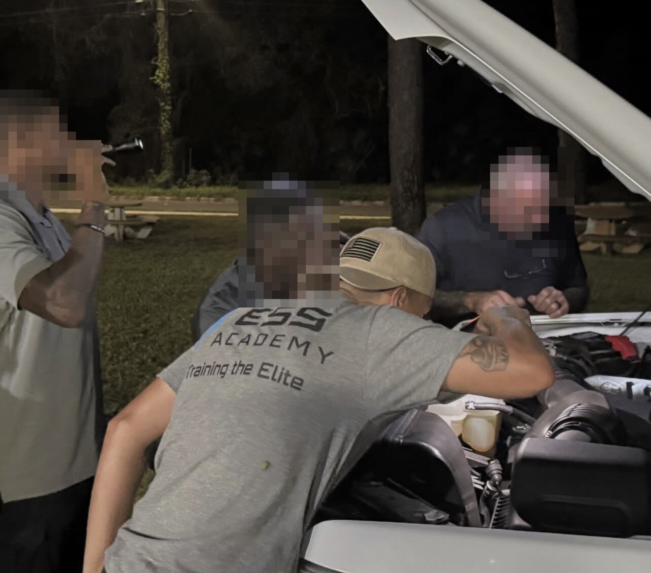 Devin Fred inspecting a vehicle engine bay at night during ESS Academy training; other trainees' faces blurred